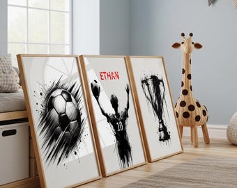 Op de afbeelding: Drie ingelijste kunstprints met een sportthema. De eerste print toont een zwart-witte voetbal met dynamische penseelstreken. De tweede print toont een voetballer met de naam "ETHAN" in het rood. De derde print toont een trofee.