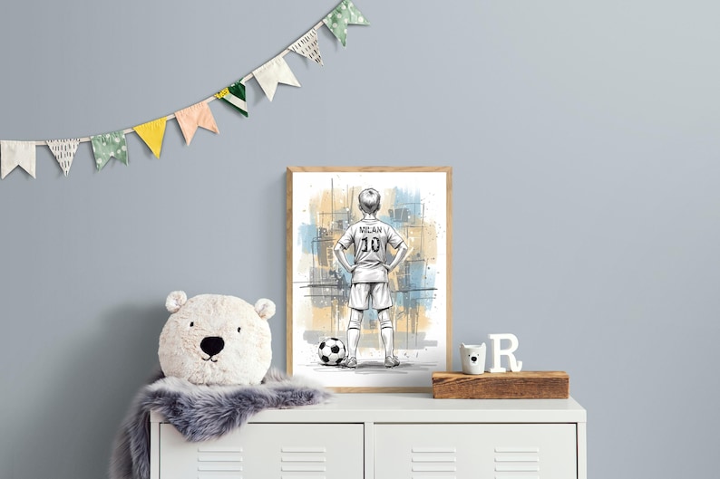 May include: A framed art print featuring a sketch of a soccer player in a Milan jersey with the number 10. A soccer ball is at the player's feet. The artwork is displayed on a white cabinet with a plush bear, a wooden block, and decorative flags.