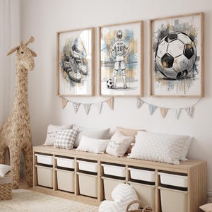 May include: Three framed watercolor prints with a soccer theme. One shows soccer cleats, another a soccer player, and the third a soccer ball. The prints are in wooden frames and hang above a storage bench with white bins.