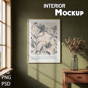 Könnte beinhalten: Ein gerahmter Druck einer botanischen Illustration von weißen Lilien mit grünen Blättern auf einem hellrosa Hintergrund. Der Druck trägt den Titel "Nature's Symphony" und ist Teil einer Blumenserie. Der Druck hängt an einer grünen Wand über einem Holz-Beistelltisch mit einer Vase mit Trockenblumen.