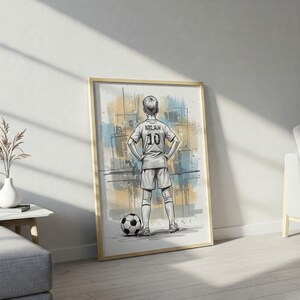 May include: Framed art print of a soccer player in a jersey with the name "Milan" and the number "10" on the back, standing with hands on hips. A soccer ball is at the player's feet. The background has blue and yellow watercolor-style splashes.