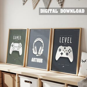 Op de afbeelding: Drie ingelijste wandposters met gaming-thema's. De linker poster is olijfgroen met een witte gamecontroller en de tekst GAMER MODE. De middelste poster is grijs met een witte koptelefoon en de naam ARTHUR. De rechter poster is donkergrijs met een witte gamecontroller en de tekst LEVEL UP.