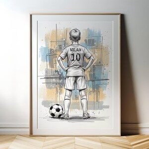 May include: Framed artwork of a soccer player in a jersey with "MILAN" and the number "10" on the back. The player stands with hands on hips next to a soccer ball. The background features abstract blue and yellow paint strokes.