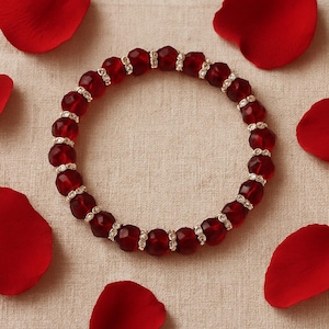 Op de afbeelding: Een cirkelvormige kralenarmband met afwisselend donkerrode gefacetteerde glaskralen en kleine zilverkleurige tussenstukjes bezet met piepkleine heldere kristallen, gerangschikt in een herhalend patroon tot een gesloten lus.