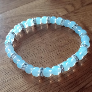 Könnte beinhalten: Ein hellblaues Perlenarmband mit silbernen Akzenten. Jede Perle ist mit kleinen Strasssteinen verziert.