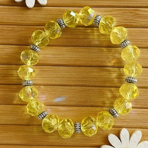 Op de afbeelding: Een gele kralenarmband met facetkralen en zilverkleurige afstandhouders. De armband is gemaakt van ronde, doorschijnende gele kralen die met elastiek aan elkaar zijn geregen. De kralen hebben een heldere, zonnige gele kleur.