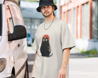 Puede incluir: Una persona lleva una camiseta beige claro con una ilustración de un gato negro y un gráfico de sol rojo. El gato está mirando hacia arriba con una expresión de sorpresa. La persona lleva un sombrero de cubo negro y un collar de cadena plateado.