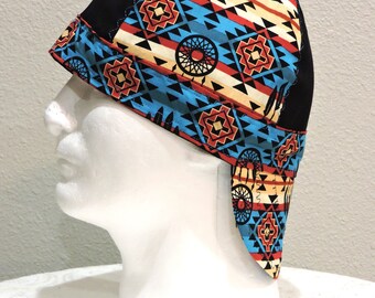 May include: A black and patterned welding cap featuring a Native American design. The cap has a black top and a brim with a geometric pattern in red, blue, and tan. The design includes dream catchers and other tribal symbols.