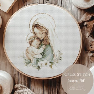 Può includere: Schema a punto croce PDF di una madre e un bambino. La madre indossa una veste blu e un velo bianco. Il bambino indossa una veste bianca e ha un'aureola. L'immagine è circondata da fiori bianchi.