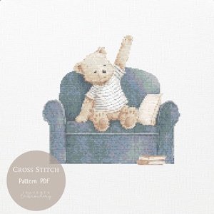 May include: A cross stitch pattern featuring a light brown teddy bear wearing a white t-shirt, sitting on a blue textured armchair with one arm raised. A small white pillow and a stack of books are beside the bear. Text reads Cross Stitch Pattern PDF.