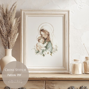 May include: A framed cross-stitch pattern featuring a mother and child, with a halo around their heads. The artwork is in soft pastel colors, framed in a distressed white wooden frame. The text "Cross Stitch Pattern PDF" is visible.