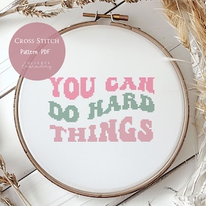 Op de afbeelding: Een kruissteekpatroon in een houten borduurring. De tekst "YOU CAN DO HARD THINGS" is gestikt in roze en groen. De woorden "Cross Stitch Pattern PDF" staan in een roze cirkel.