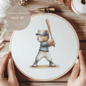 May include: Cross-stitch pattern PDF featuring a teddy bear in a baseball uniform, holding a bat. The bear is wearing a blue cap, shirt, and white pants. The design is set in a wooden embroidery hoop. Text on the image reads "Cross Stitch Pattern PDF" and "Juliette Embroidery".