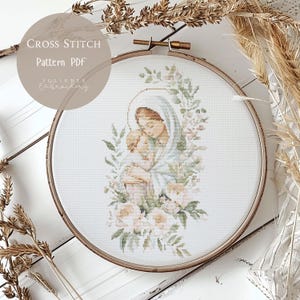 Puede incluir: Patrón de punto de cruz PDF de una pintura de acuarela de María sosteniendo al niño Jesús. La imagen está rodeada de una corona de flores con rosas rosas y hojas verdes. El patrón está disponible para descargar.