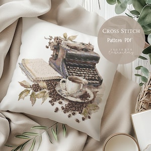 Può includere: Un cuscino bianco con un disegno a punto croce raffigurante una macchina da scrivere vintage, un libro, una tazza di caffè e chicchi di caffè. Il design è nei toni del marrone, beige e grigio. Il testo sul cuscino recita "Cross Stitch Pattern PDF" e "Juliette Embroidery".
