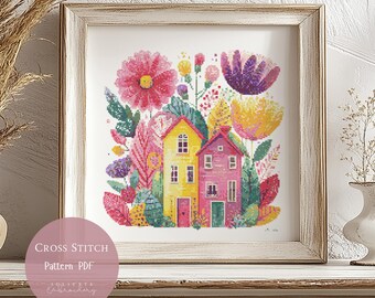 May include: Cross-stitch pattern PDF of a colorful floral and house design. The artwork features two houses, one yellow and one pink, surrounded by flowers in shades of pink, purple, and yellow. The framed art is displayed on a white surface.