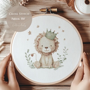 Puede incluir: Patrón de punto de cruz de un león con una corona verde, rodeado de estrellas y follaje, dentro de un bastidor de bordado de madera. El texto en la imagen dice "Cross Stitch Pattern PDF" y "Juliette Embroidery".