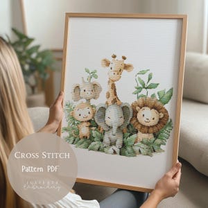 Puede incluir: Un patrón de punto de cruz enmarcado que presenta una encantadora escena de la jungla con una jirafa, un elefante, un león, un mono y otros animales. La obra de arte está sobre un fondo blanco y enmarcada en madera clara. El texto "CROSS STITCH Pattern PDF" es visible.