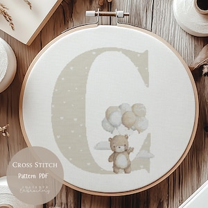 May include: A cross-stitch pattern in a wooden hoop features a large letter "C" in a light beige color, decorated with small white hearts. A teddy bear holds balloons. The text "CROSS STITCH Pattern PDF" is visible.