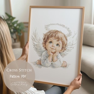 Può includere: Schema a punto croce PDF di un adorabile angelo con un'aureola, ali e un'espressione dolce. L'angelo è seduto con le mani giunte sotto il mento. Lo schema è in tonalità di bianco, marrone e beige.