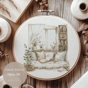 Könnte beinhalten: Ein Kreuzstichmuster in einem Holzrahmen zeigt eine gemütliche Fenstersitzszene. Das Design zeigt ein Fenster mit Vorhängen, Topfpflanzen, ein Bücherregal und Kissen. Der Text "Cross Stitch Pattern PDF" ist sichtbar.