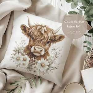 May include: Cross stitch pattern PDF for a Highland cow with white flowers. The pattern is available for download.  The image shows a pillow with the finished cross stitch design.