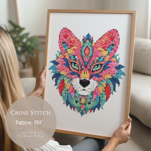 May include: A framed cross-stitch pattern of a colorful fox head. The artwork features a detailed design with pink, blue, green, and yellow hues. The text "CROSS STITCH Pattern PDF" is visible on the image, along with the artist's name.