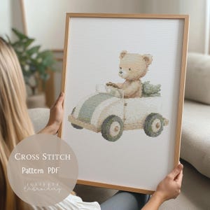 May include: A framed cross-stitch pattern featuring a teddy bear driving a white car with green stripes. The artwork is in a wooden frame. The text "CROSS STITCH Pattern PDF" and the artist's name are visible.