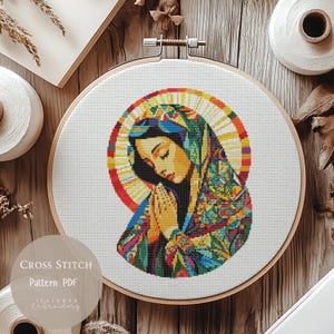 May include: A cross stitch pattern PDF of a colourful, abstract depiction of the Virgin Mary praying. The image is in a circular embroidery hoop.