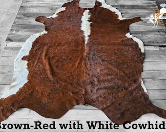 May include: Brown-red cowhide rug with white patches. The rug is laid out on a wooden floor.