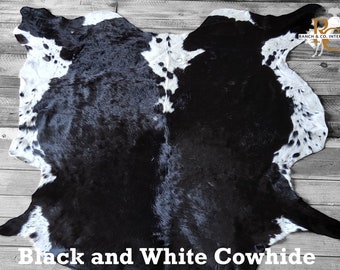 May include: A black and white cowhide rug with a natural shape. The rug has a mix of black and white patches, with the text "Black and White Cowhide" at the bottom. The rug is displayed on a wooden surface.