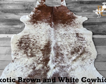 May include: An exotic brown and white cowhide rug. The rug has a natural shape with a mix of brown and white spotted patterns. The text "Exotic Brown and White Cowhide" is at the bottom of the image.