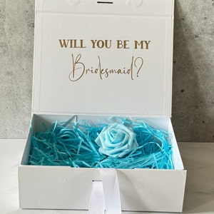 Peut inclure: Bo&icirc;te blanche avec un ruban bleu et une rose bleu clair &agrave; l'int&eacute;rieur. La bo&icirc;te porte l'inscription "Veux-tu &ecirc;tre ma demoiselle d'honneur ?" sur le couvercle.