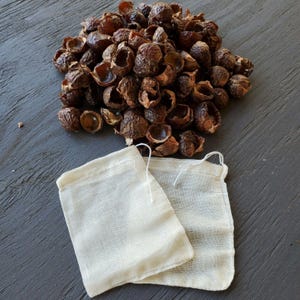 May include: A pile of brown soap nuts with two white mesh laundry bags. The soap nuts are a natural alternative to laundry detergent.