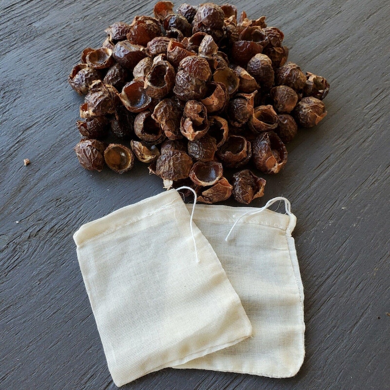 May include: A pile of brown soap nuts with two white mesh laundry bags. The soap nuts are a natural alternative to laundry detergent.