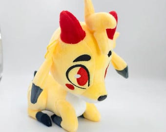 May include: A yellow plush creature with red horns, large red eyes, and black accents on the ears and feet. The soft toy features a white chest patch, a small red cheek mark, and a tuft of yellow hair on top of its head, posed in a sitting position.