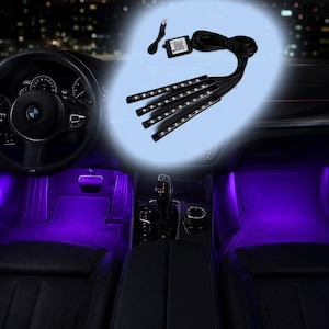 May include: Car interior illuminated with purple LED lights, highlighting the footwells and dashboard. The image shows a car's interior, including the steering wheel, seats, and center console. The lighting kit includes light strips and a control module.