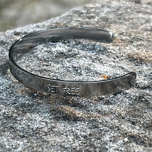 May include: A silver metal bracelet with the words "Set Free" engraved on the band.