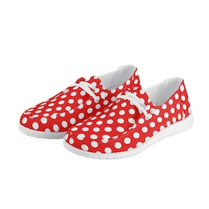 May include: A pair of red canvas slip-on shoes with white polka dots. The shoes have white laces and a white sole.