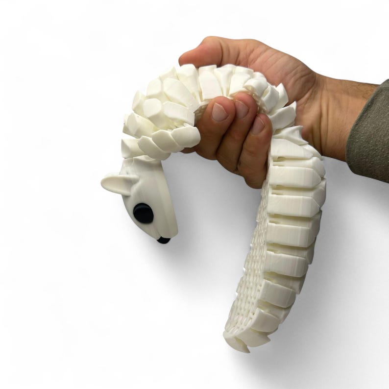 May include: A white articulated pangolin toy with a segmented body and a head with black eyes and small ears. The toy is held in a person's hand against a white background. The pangolin's body is made of many small, rectangular segments.