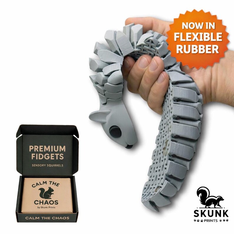 Gray flexible 3D printed squirrel fidget toy shown bending in a hand, featuring articulated segments and a rubber-like material for sensory play. Product image includes premium gift box packaging with “Premium Fidgets” and “Calm the Chaos” branding, Skunk Prints logo, and a sticker that reads “Now in Flexible Rubber.” Designed for sensory seekers, ADHD, autism, stress relief, and quiet desk fidgeting.