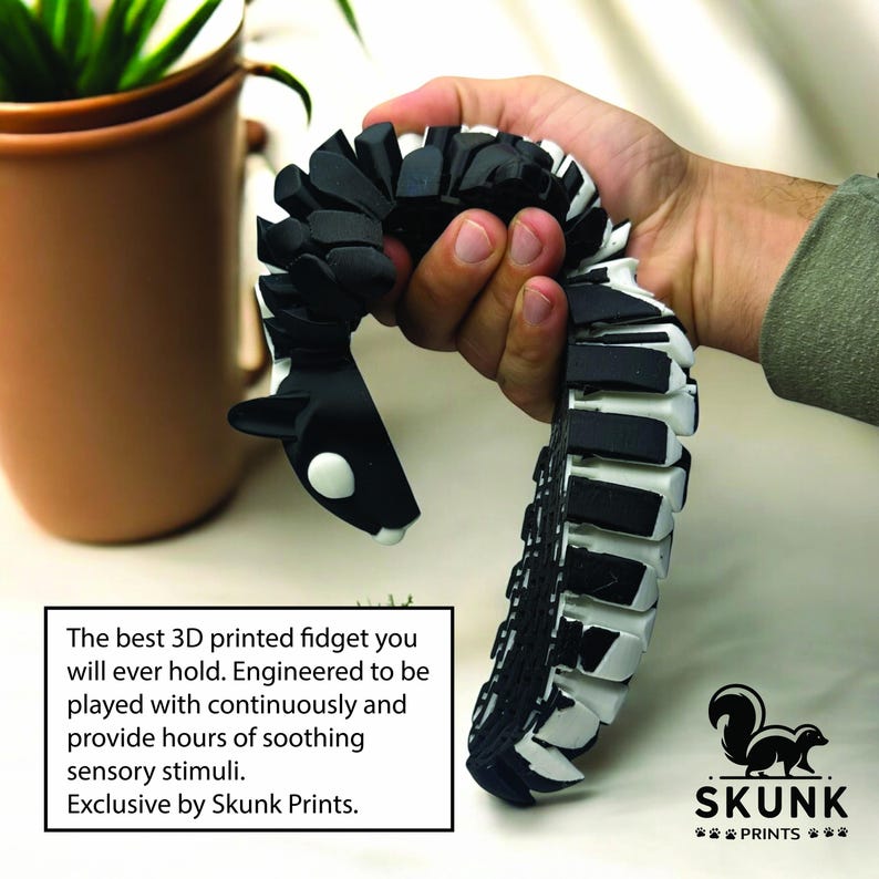May include: A black and white 3D-printed fidget toy, held in a hand. The toy is shaped like a snake or worm, with articulated segments. The text on the image says: "The best 3D printed fidget you will ever hold."