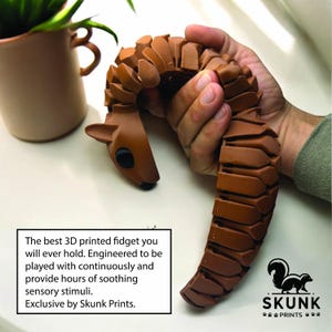 May include: A brown 3D-printed fidget toy shaped like a deer, held in a person's hand. The text on the image reads: "The best 3D printed fidget you will ever hold. Engineered to be played with continuously and provide hours of soothing sensory stimuli. Exclusive by Skunk Prints."