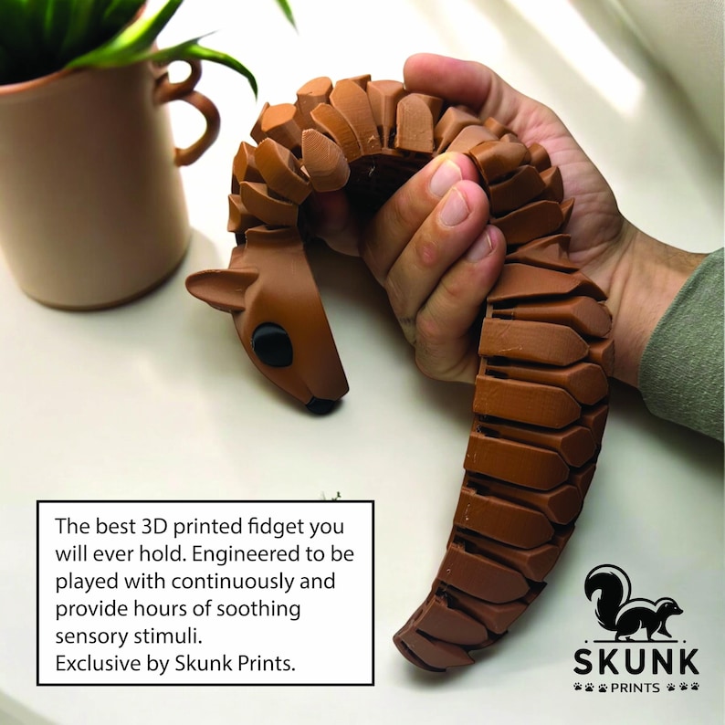 May include: A brown 3D-printed fidget toy shaped like a deer, held in a person's hand. The text on the image reads: "The best 3D printed fidget you will ever hold. Engineered to be played with continuously and provide hours of soothing sensory stimuli. Exclusive by Skunk Prints."