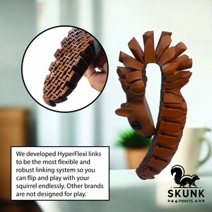 May include: A brown, flexible dog toy shaped like a squirrel, with a detailed textured design. The toy has a head and tail, and the text "SKUNK PRINTS" is visible. The toy is designed for dogs to flip and play with.