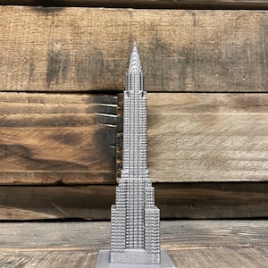 Peut inclure: Une maquette argentée du Chrysler Building, un gratte-ciel célèbre de New York. La maquette est détaillée et présente une surface texturée.