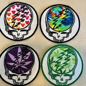 May include: Four round embroidered patches featuring the Grateful Dead's iconic Steal Your Face skull logo. Each patch has a different design: a tie-dye pattern, a purple and green marijuana leaf design, a green marijuana leaf design, and a rainbow design with hearts.