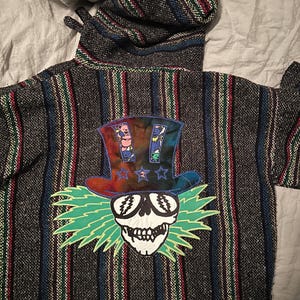 May include: A black and grey striped hooded sweatshirt with a colourful Grateful Dead Steal Your Face patch on the back. The patch features a skull with sunglasses, a top hat, and green lightning bolts.
