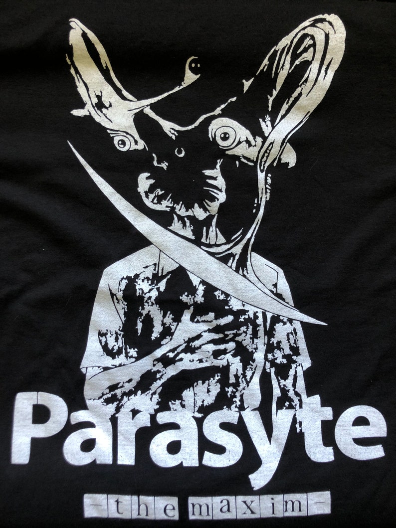 May include: Black t-shirt featuring a white graphic of a creature with large ears and a blade. The text "Parasyte" is above "the maxim" in a white font.