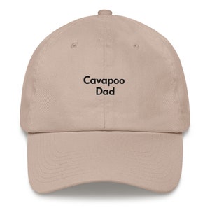 Op de afbeelding: Een beige baseballpet met zwarte geborduurde tekst die "Cavapoo Dad" luidt.